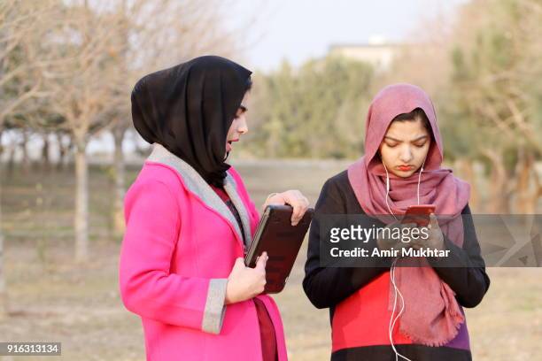 two beautiful young girls in hijab (head scarf) walking and talking in the park at day time while holding a laptop and cell phone. - punjabi girls images 個照片及圖片檔