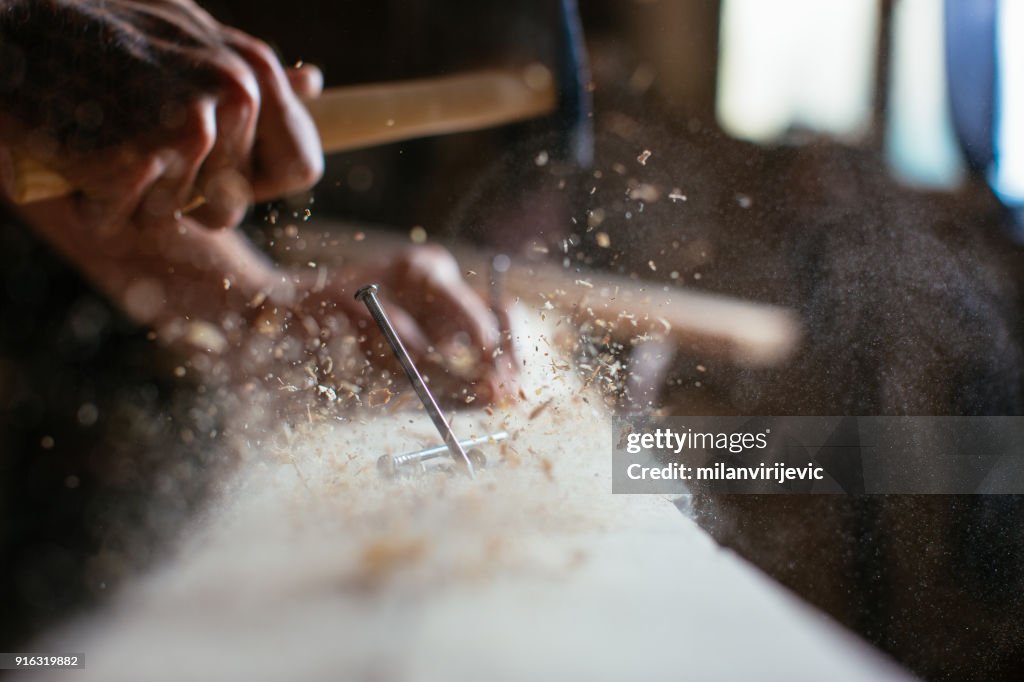Close up of man hammering a nail into wooden board