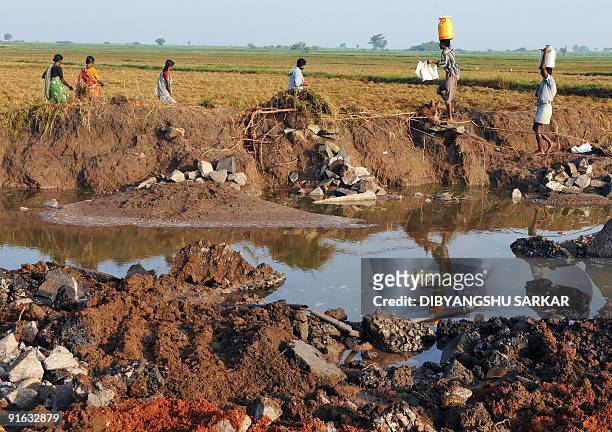 Indian villagers walk past a flood damaged road in the village of Makthal in Meboob Nagar District some 660kms north of Bangalore on October 9, 2009....