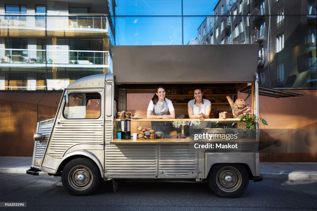 Portrait of female owners in food truck parked on city street against building