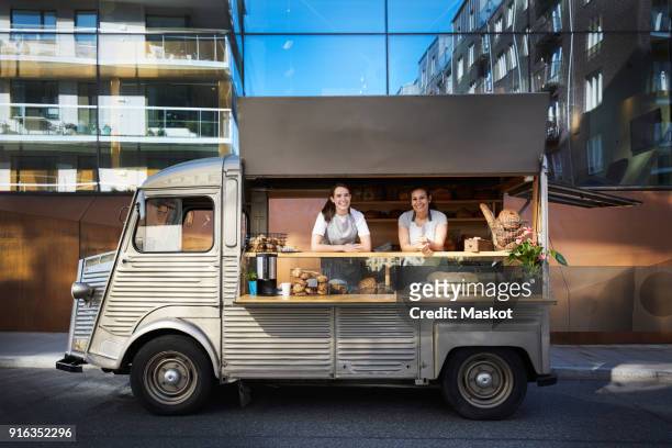 portrait of female owners in food truck parked on city street against building - foodtruck stockfoto's en -beelden