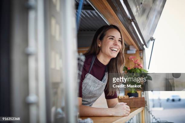 smiling young woman looking away while standing in food truck at city - foodtruck stockfoto's en -beelden