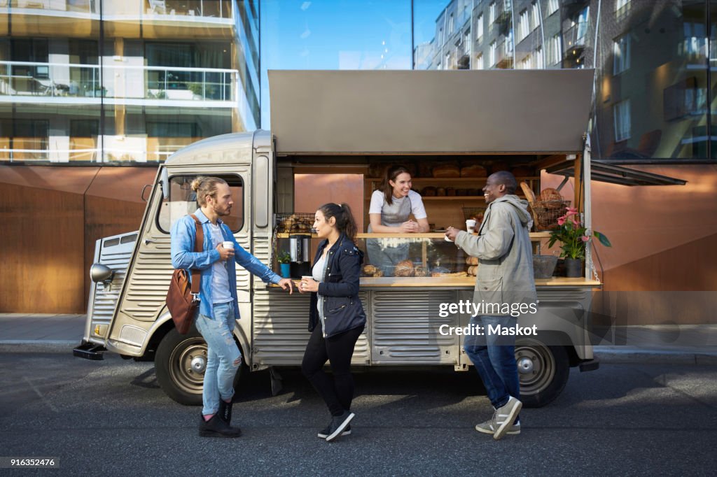 Female owner in concession stand while customers having food and drink on street in city