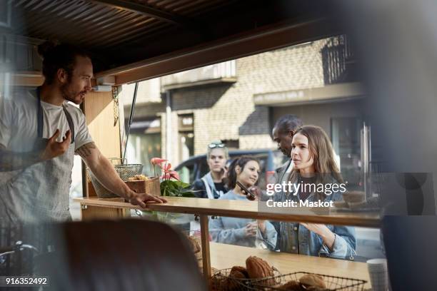 young male owner taking order from female customer at food truck in city - kiosk stock-fotos und bilder