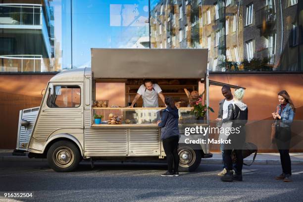 multi-ethnic customers buying from owner in food truck against building - furgone ambulante foto e immagini stock