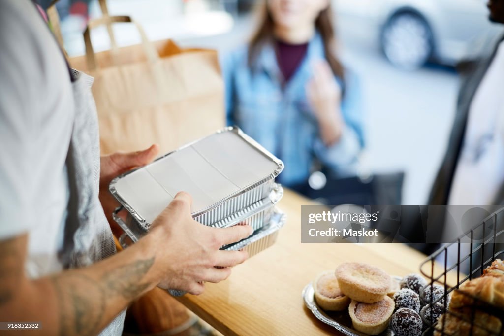 Midsection of salesman holding takeaway packaged food for customers at concession stand