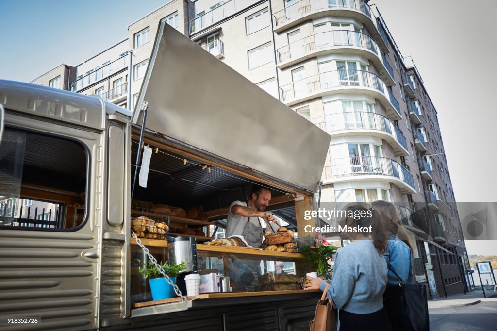 Female customers buying bread from salesman at food truck in city