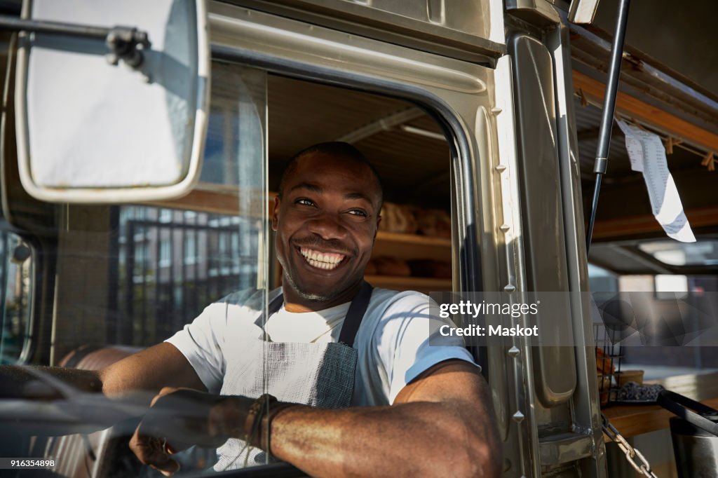 Smiling mid adult salesman looking away while driving food truck in city