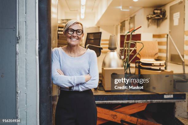 portrait of smiling mature businesswoman standing arms crossed in new office - moving office stock pictures, royalty-free photos & images