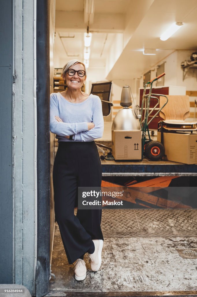 Full length portrait of smiling mature businesswoman standing arms crossed in new office