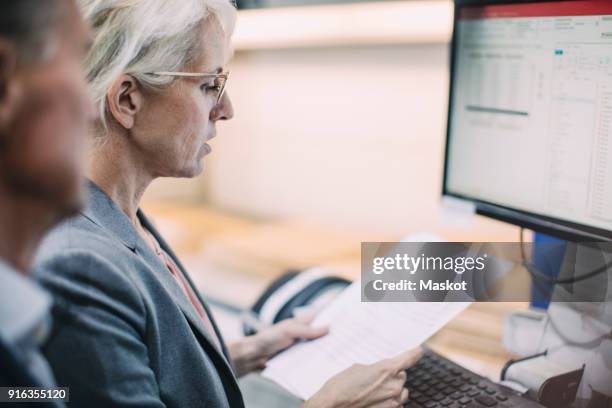 businesswoman reading document while standing in front of desktop computer with colleague at industry - purchase order stock pictures, royalty-free photos & images