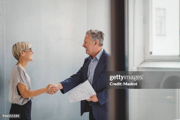 mature businessman and businesswoman shaking hands in new office - moving office stock-fotos und bilder