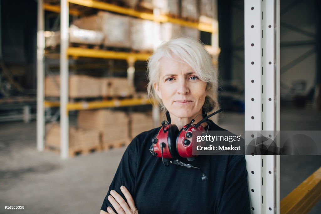 Close-up of smiling worker standing with arms crossed by rack of industry