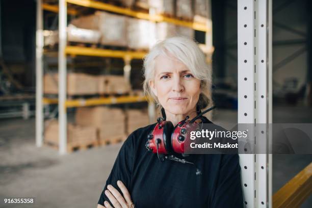 close-up of smiling worker standing with arms crossed by rack of industry - protective workwear for manual worker stockfoto's en -beelden