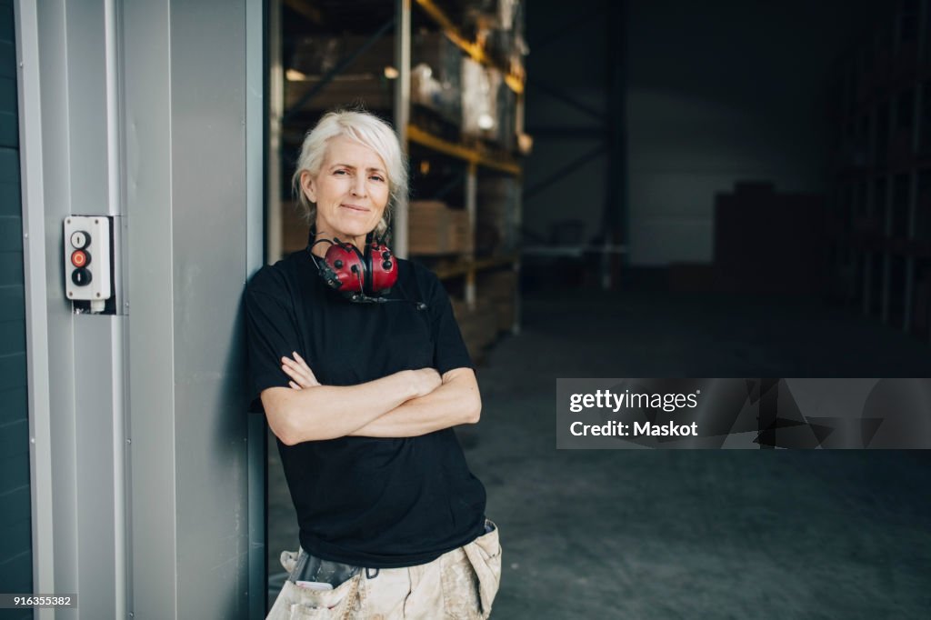 Smiling worker standing with arms crossed at entrance of industry