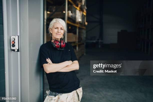 smiling worker standing with arms crossed at entrance of industry - entrance building people stock pictures, royalty-free photos & images