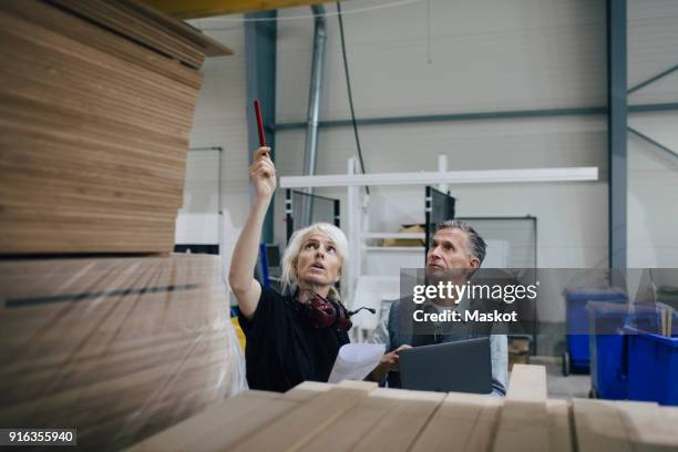 mature woman discussing with colleague while examining wooden planks at industry - holzbau stock-fotos und bilder