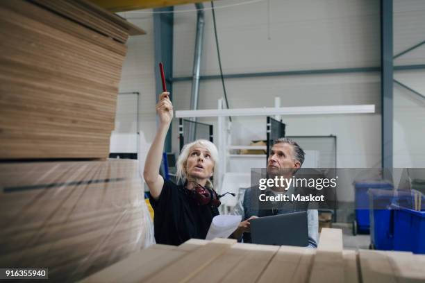 mature woman discussing with colleague while examining wooden planks at industry - madera material de construcción fotografías e imágenes de stock