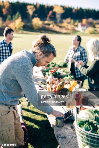 male farmer using digital tablet at table with friends in background - man lady phone ipad outside stock pictures, royalty-free photos & images