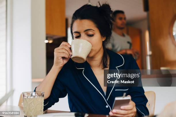 woman drinking coffee while looking at glaucometer by table - glaucometer stockfoto's en -beelden