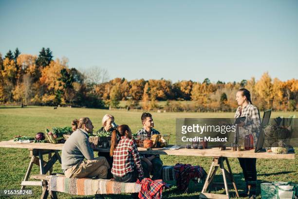 instructor holding digital tablet while talking with farmers sitting at table on field - standing table outside stock pictures, royalty-free photos & images