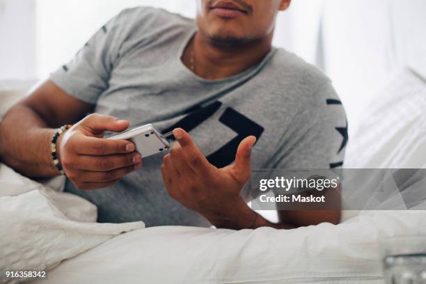 midsection of man checking blood sugar level on glaucometer while lying on bed at home - glaucometer stockfoto's en -beelden