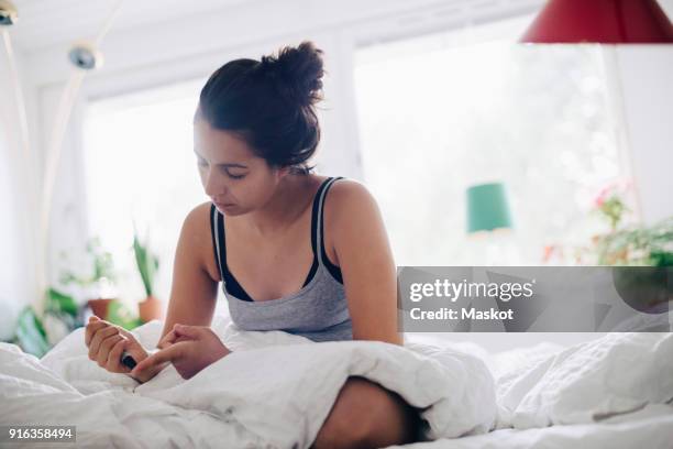 woman checking blood sugar level while sitting on bed - diabetes lifestyle stock-fotos und bilder