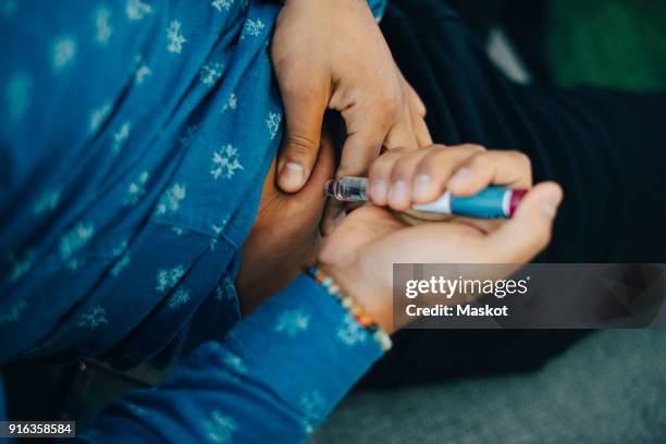 midsection of businessman injecting insulin in abdomen while sitting on sofa - injecting stomach stock pictures, royalty-free photos & images