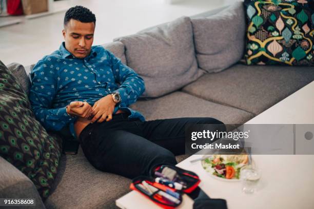 businessman injecting insulin in abdomen while sitting on sofa in office - injecting stomach stock pictures, royalty-free photos & images