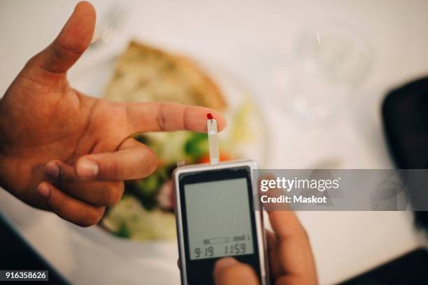 businessman using glaucometer in blood test while having food at table - glaucometer stock pictures, royalty-free photos & images