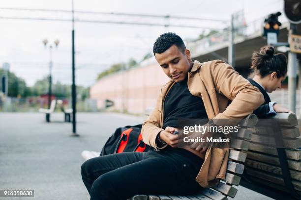 man injecting insulin in abdomen while sitting on bench at railroad station platform - typ 1 diabetes stock-fotos und bilder