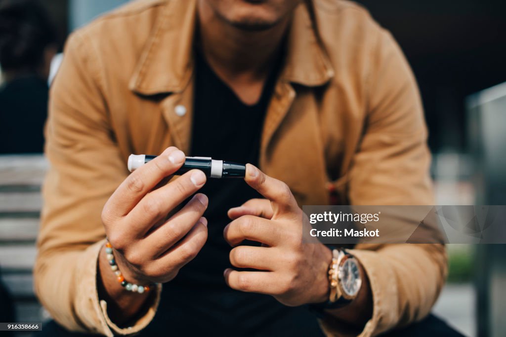 Midsection of man doing blood test while sitting on bench