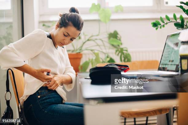 businesswoman injecting insulin while sitting at desk in office - injecteren stockfoto's en -beelden