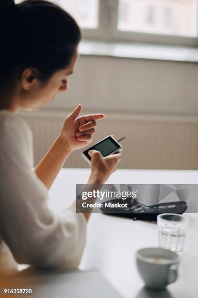close-up of woman checking blood sugar level in glaucometer while sitting at table - glaucometer stockfoto's en -beelden
