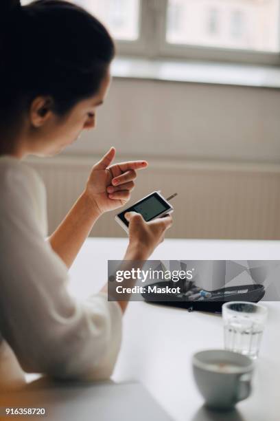 close-up of woman checking blood sugar level in glaucometer while sitting at table - glaucometer stock pictures, royalty-free photos & images