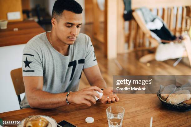 man taking pills while having breakfast at table - taking medication stockfoto's en -beelden