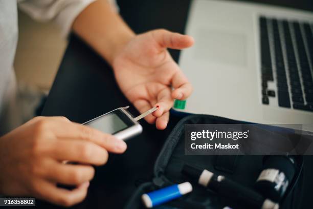 cropped hands of businesswoman checking blood sugar level with glaucometer at desk - glaucometer stockfoto's en -beelden