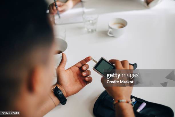 businessman checking blood sugar level with glaucometer at table - glaucometer stockfoto's en -beelden