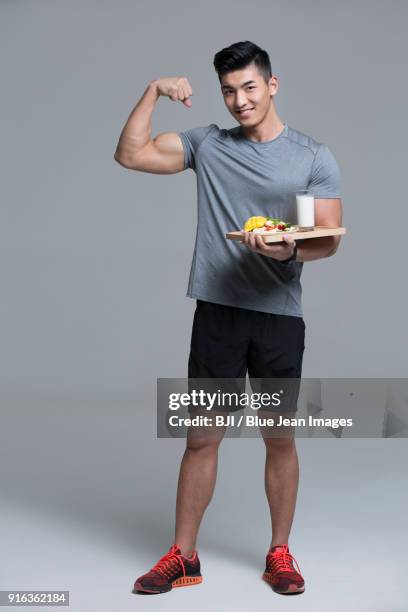 young male athlete flexing muscles while holding vegetable salad and milk - flexing muscles foto e immagini stock