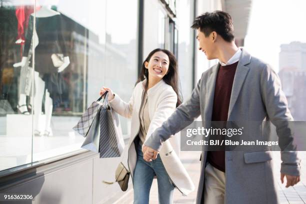 cheerful young couple holding hands walking with shopping bags - couple shopping in shopping mall stockfoto's en -beelden