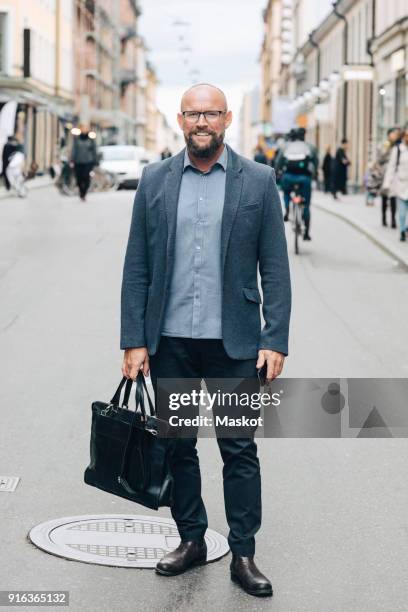 full length of smiling mature businessman standing on city street - マンホール ストックフォトと画像