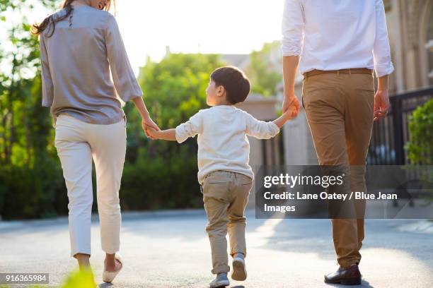 happy young family holding hands walking - dreiviertel rückansicht stock-fotos und bilder