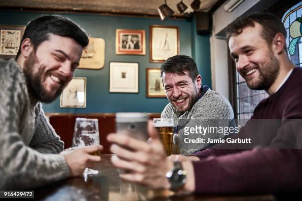 three british males sat together looking at a phone together laughing at it. - three people at table stock pictures, royalty-free photos & images