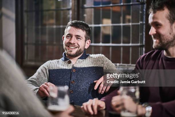 portrait of bearded male sat smiling with his friends at a table of a pub with his friends - pub mates stock-fotos und bilder