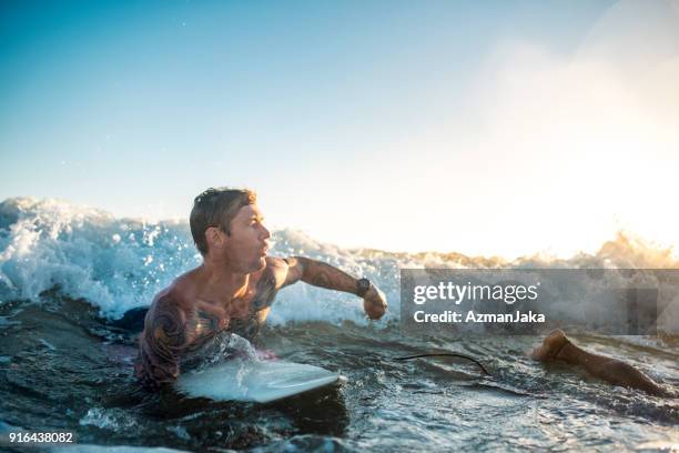 man with tattoos on a surfboard in the ocean - gold coast surfing stock pictures, royalty-free photos & images