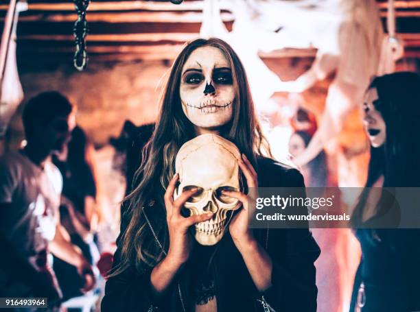 young woman with skeleton make-up holding skull at halloween party - halloween zombie makeup imagens e fotografias de stock