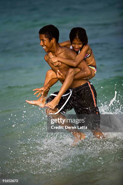 brother and sister piggy back running in water - derek latta stock pictures, royalty-free photos & images