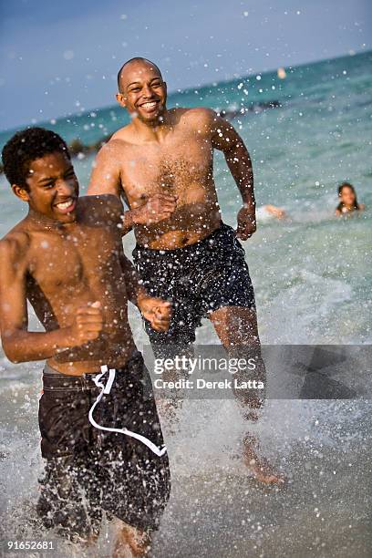 father and son running through water on beach - derek latta stock-fotos und bilder