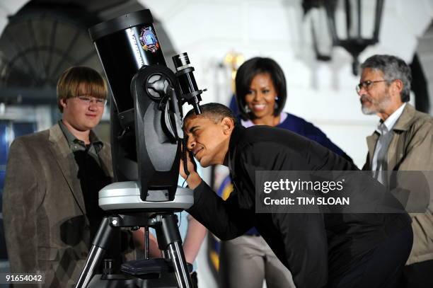 President Barack Obama with his wife Michelle and Science Advisor John Holdren looks through a telescope during an event for local middle school...