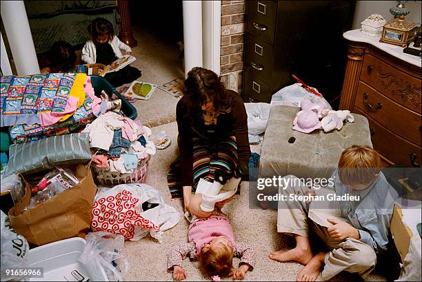 Allie, one of three wives in a polygamist family of 21 children changes 2-year-old Vanessa's diaper after having folded some laundry. Two washers and...